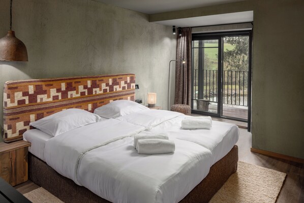 A large bed with white linens and two towels, a patterned headboard, a nightstand with a lamp, and a view of the outdoors through a sliding glass door. - Roompot Hillview Resort Grandvoir (Neufchateau)