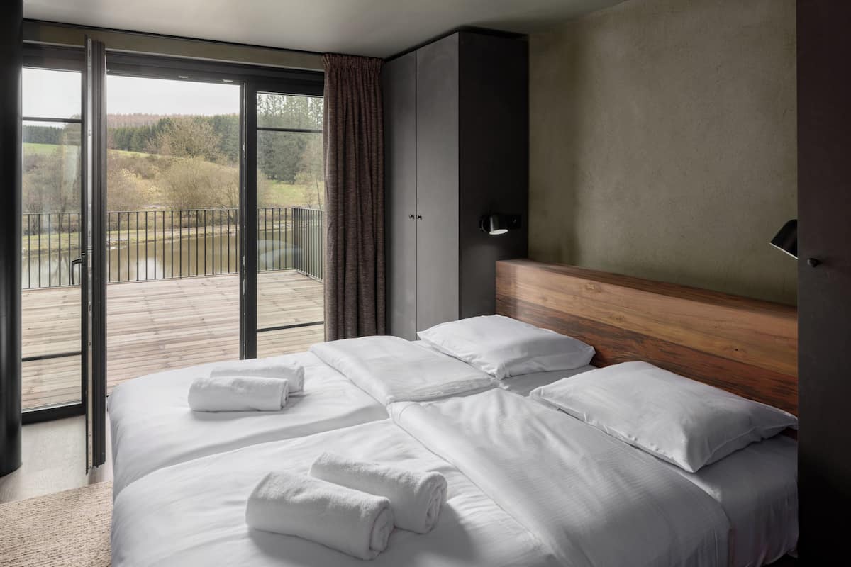 Een hotelkamer met een groot bed, een houten hoofdbord en uitzicht op een balkon met een hekwerk.