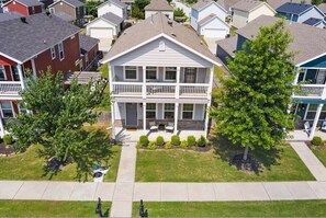 A two-story house with a front porch and a small deck, surrounded by a well-maintained lawn and trees.