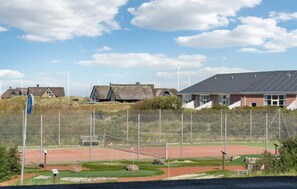 A golf course with a fenced area, a building with a thatched roof, and a clear sky. - Awesome apartment in Fanø with WiFi (Fanø)