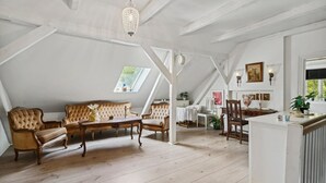 A spacious attic room with a high ceiling, wooden beams, a large window, a sofa, a table, and various decorative items.