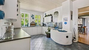 A modern kitchen with white cabinets, a curved island, and a view of greenery outside.