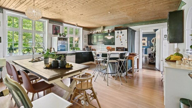 A spacious kitchen with wooden floors, a dining area with a table and chairs, and a view of the outdoors through large windows.