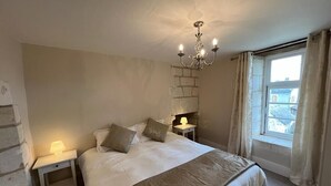 Un dormitorio con cama, mesitas de noche, un candelabro, una ventana con cortinas y una pared de piedra.