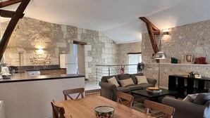Amplia sala de estar con una mesa de comedor de madera, un conjunto de sofás y una cocina con un fondo de pared de piedra.