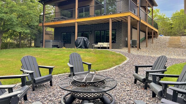 Ett modernt hus i två våningar med en täckt uteplats, inredd med Adirondack-stolar och en eldstad.