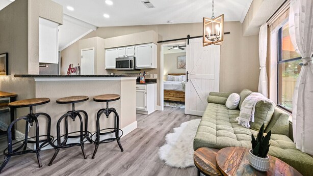 A modern kitchen with white cabinets, a central island with stools, a dining area with a wooden table, and a cozy living room with a green sofa and a white fur rug. - `Saloma Place` Pet-Friendly! Large yard! Work Space! (Austin)