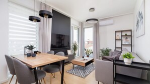 Una sala de estar moderna con una mesa de comedor de madera, sillas grises, un televisor de pantalla plana y un sofá gris.