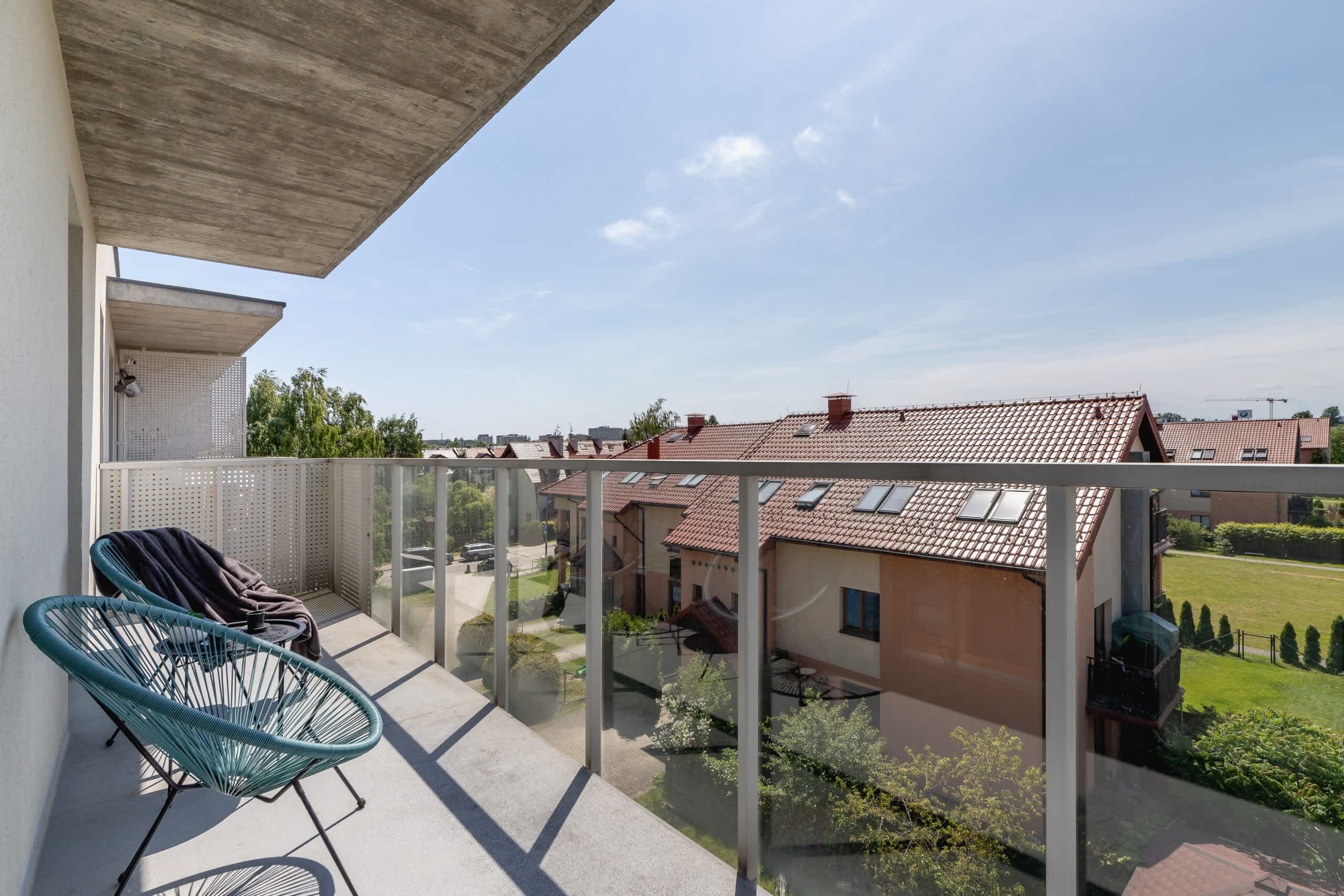 Un balcon doté d’une balustrade en verre, une chaise bleue et une vue sur les maisons voisines.