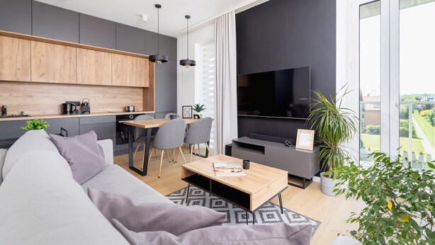 Una sala de estar moderna con un sofá, una mesa de centro y un televisor. Hay una zona de cocina con armarios y una mesa de comedor.