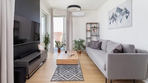 Una sala de estar moderna con televisor de pantalla plana, sofá gris, mesa de centro de madera y un cuadro en la pared.