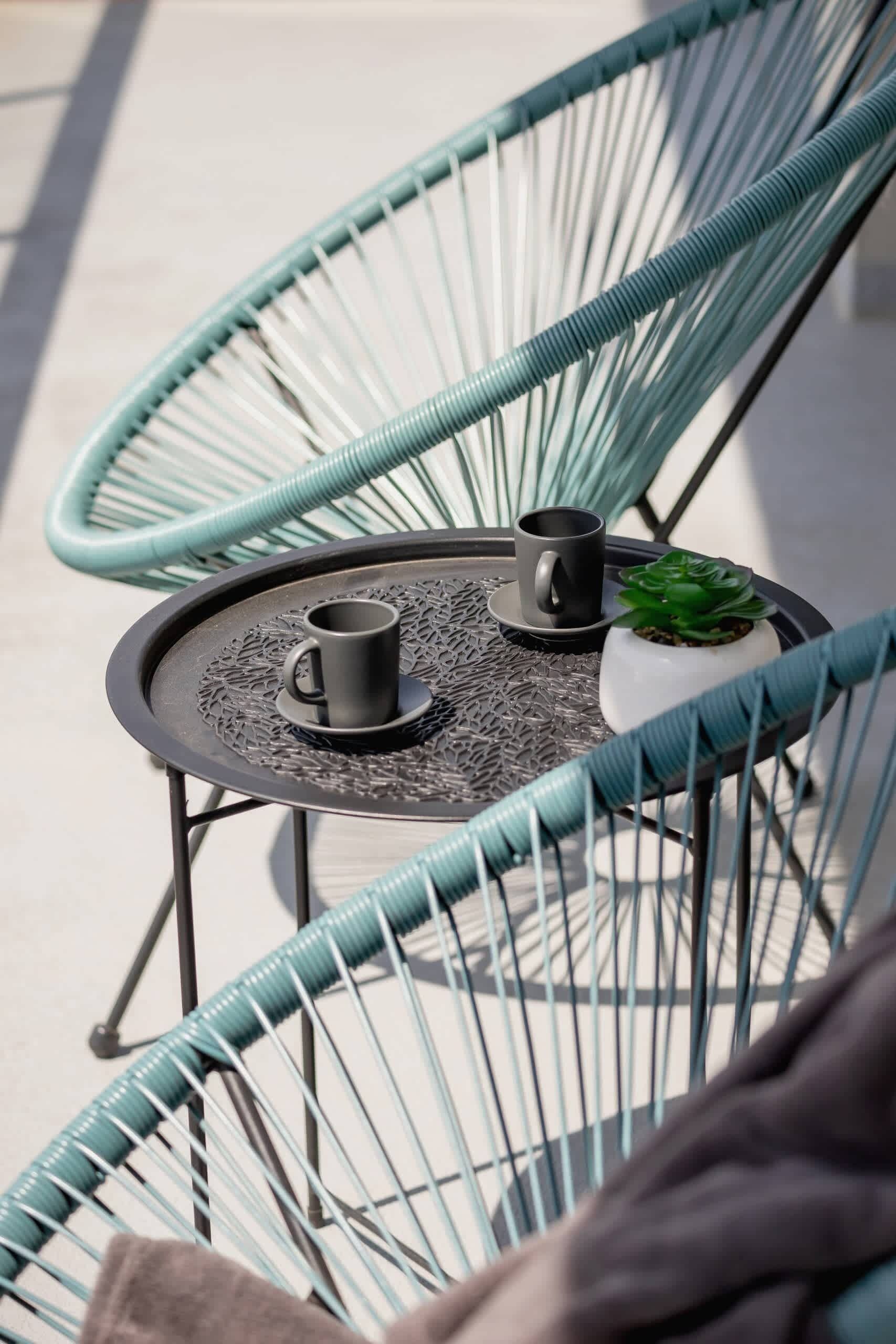 A round table with a black metal frame, two black cups, and a small potted plant.