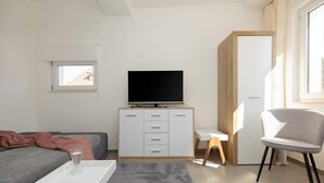 Un dormitorio moderno con cama, televisor sobre una cómoda, una ventana pequeña y una silla.