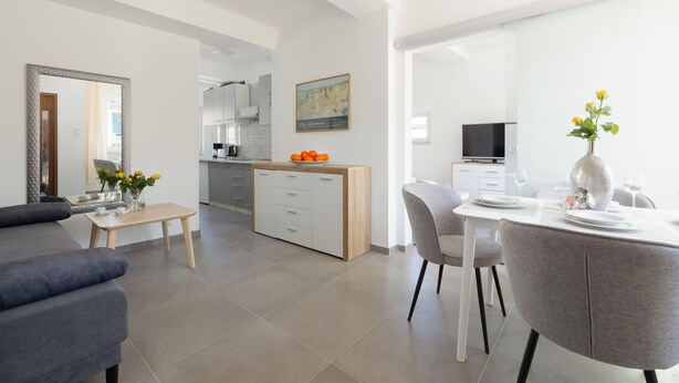 Una sala moderna con sofá, mesa de comedor con sillas, zona de cocina y televisor.