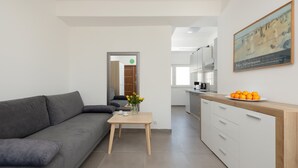 Una sala de estar moderna con un sofá gris, una mesa de centro de madera y una cocina con armarios blancos y encimera de madera.