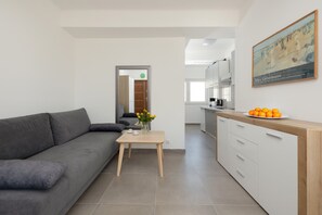 A modern living room with a grey sofa, a wooden coffee table, and a kitchen area with white cabinets and a wooden countertop.
