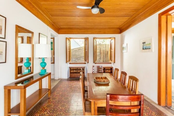 A dining area with a long wooden table, chairs, a ceiling fan, and patterned flooring.
