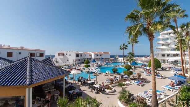 A resort with a swimming pool, outdoor seating, and palm trees.