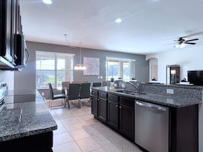 A modern kitchen with granite countertops, a central island, and a dining area with chairs.