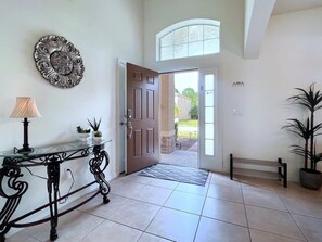 A spacious entrance with a glass door, a metal console table with a lamp, and a potted plant.
