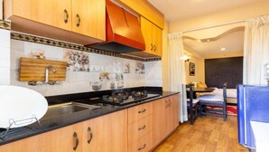A compact kitchen with wooden cabinets, a black countertop, and a sink. There is a dining area with a table and chairs visible in the background. - MeroStay 190 HOMESTAY (Sainbu)