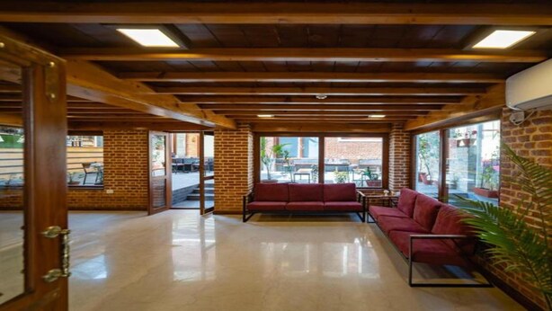 A spacious lobby with a red sofa, wooden beams, brick walls, and large windows offering a view of the street. - MeroStay 190 HOMESTAY (Sainbu)