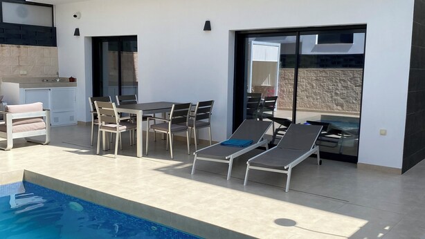 A modern outdoor pool area with a dining set and lounge chairs. - Modern villa in a quiet location (Benijofer)