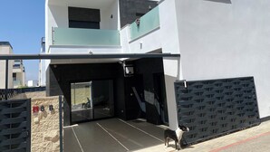 A modern two-story building with a garage entrance, a dog standing outside, and a clear blue sky. - Modern villa in a quiet location (Benijofer)