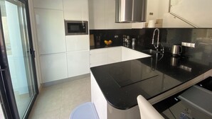 A modern kitchen with white cabinets, a black countertop, stainless steel appliances, and a glass door leading to a balcony. - Modern villa in a quiet location (Benijofer)