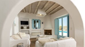 A cozy room with a fireplace, a TV, and a view of the sea. - Eden's Mykonos - Villa Opal (Mykonos)