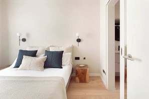 A bedroom with a bed, pillows, a nightstand, a wall-mounted lamp, and a door leading to a closet.