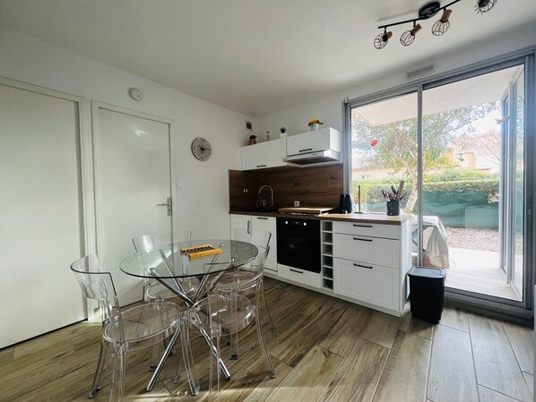 Une cuisine moderne avec une table et des chaises en verre, un plancher en bois et une vue sur l’extérieur grâce à une porte-fenêtre coulissante.