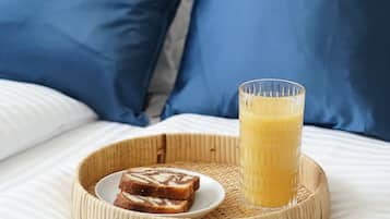 A bed with blue pillows, a tray with toast and a glass of orange juice.