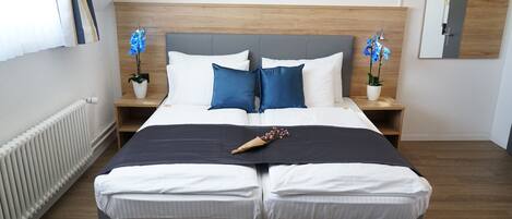 Un dormitorio moderno con una cama grande, cabecera de madera, dos mesitas de noche con orquídeas azules y un espejo en la pared.