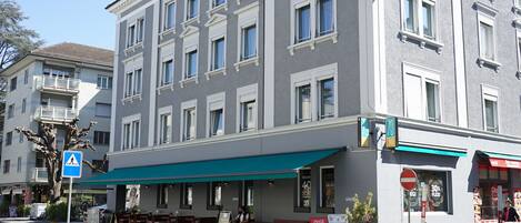 A multi-story hotel with a green awning, a pedestrian crossing sign, and a no entry sign.