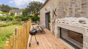 A patio with a barbecue grill, outdoor seating, and a stone wall. - Charming Stone Barn Near the Sea (Bretteville)