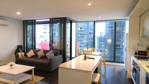 A modern apartment with a living area, kitchen, and large windows offering city views. - ReadySet Apartments at Manhattan (Melbourne)