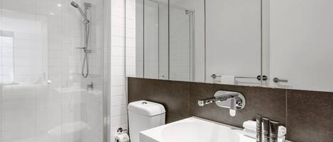 Un baño moderno con cabina de ducha de vidrio, inodoro blanco, tocador con espejo y lavamanos.