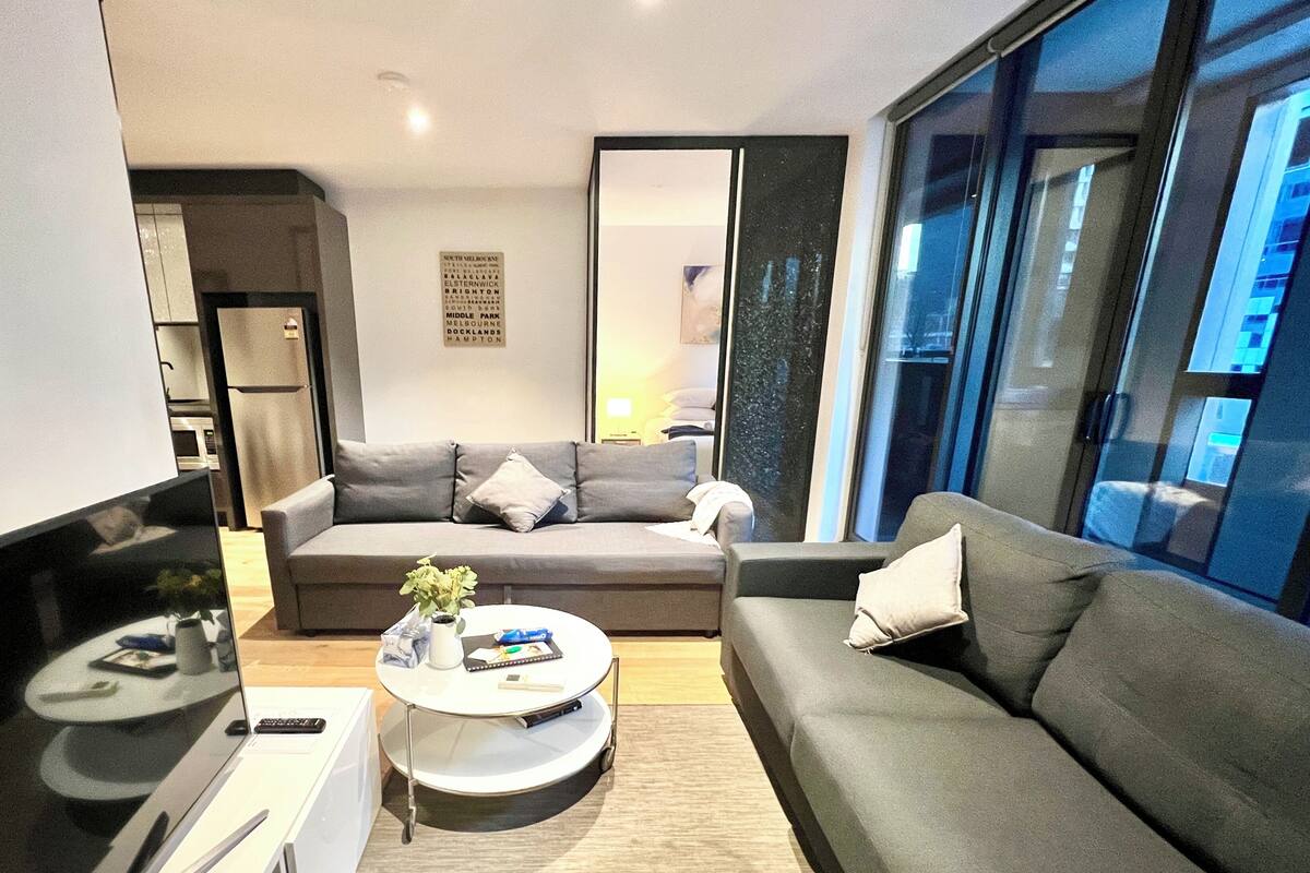 Un salon moderne avec un canapé gris, une petite table basse et une grande fenêtre.