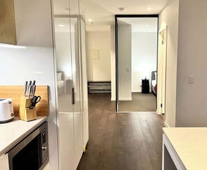 A modern kitchen with a refrigerator, microwave, and a wooden utensil holder. - ReadySet Apartments at Manhattan (Melbourne)