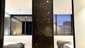 A modern hotel room with a large window, a bed, a sofa, and a decorative wall panel. - ReadySet Apartments at Manhattan (Melbourne)