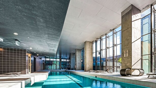 An indoor swimming pool with clear blue water, large windows, and modern architecture. - ReadySet Apartments at Manhattan (Melbourne)