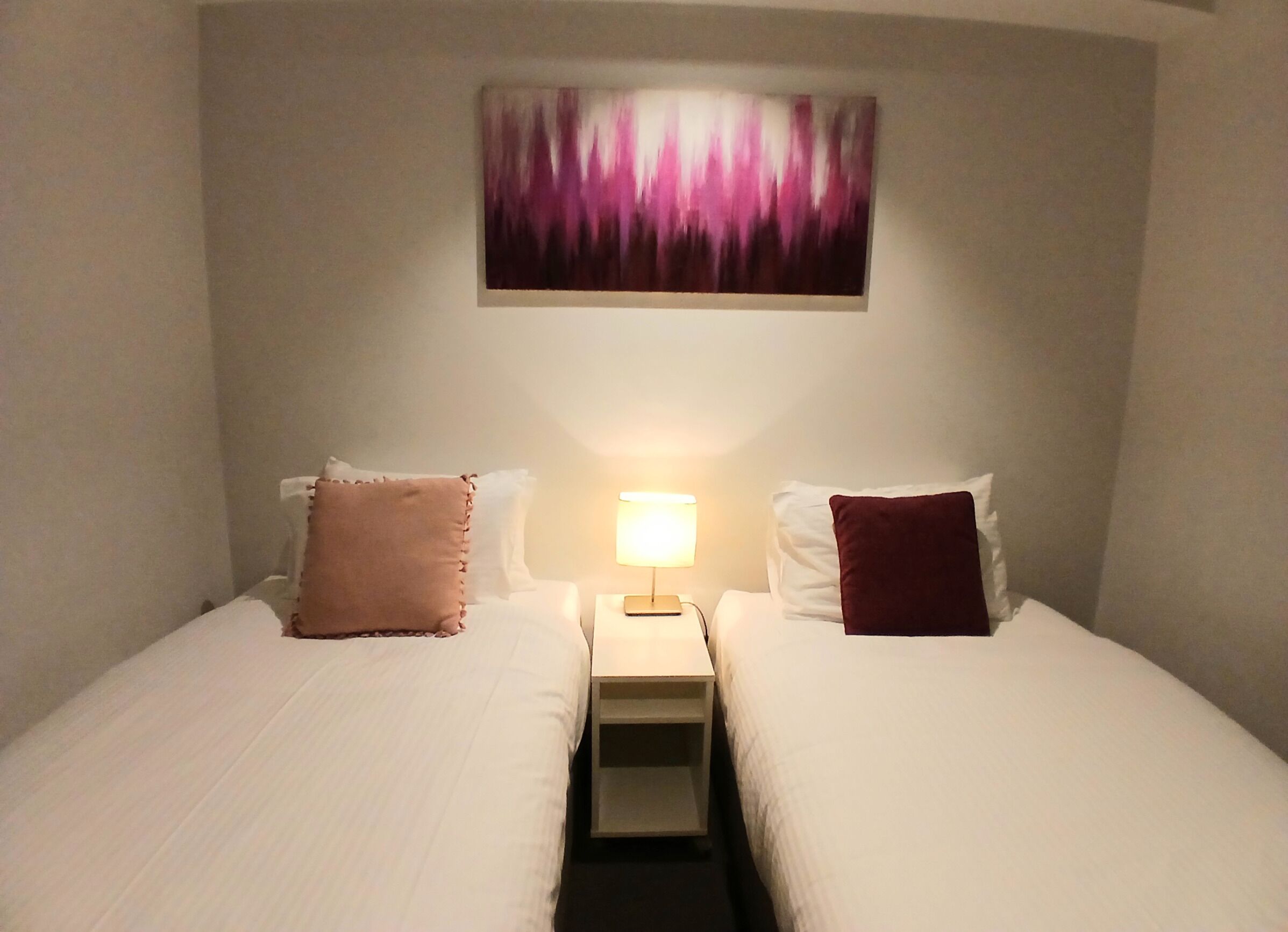 A hotel room with two beds, a nightstand with a lamp, and a painting on the wall.