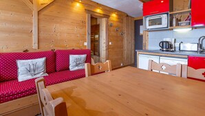 Un accogliente interno di una baita con arredamento in legno, un divano rosso con cuscini decorati, un tavolo da pranzo in legno e un angolo cottura con un pensile rosso e un forno a microonde.