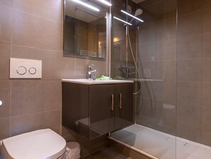 A modern bathroom with a glass-enclosed shower, a white toilet, and a dark cabinet with a mirror above the sink. - 3-room apartment for 6 in the heart of Avoriaz (Avoriaz)