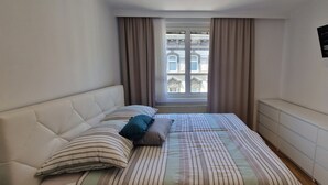 A bedroom with a bed, pillows, a window with curtains, and a radiator.