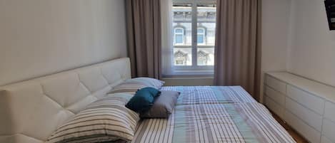 A bedroom with a bed, pillows, a window with curtains, and a radiator.