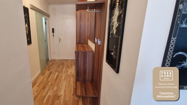 A hallway with wooden flooring, a white door, and a wooden wardrobe.
