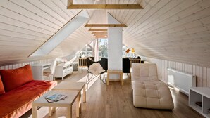 Une chambre aménagée dans les combles, avec un plafond en pente, des poutres apparentes, un bureau blanc, un canapé, une chaise et un radiateur.