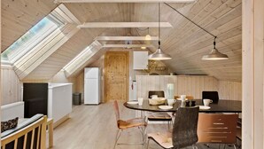 Une pièce confortable aménagée comme un grenier, avec un intérieur en bois, une table à manger avec des chaises et un réfrigérateur.
